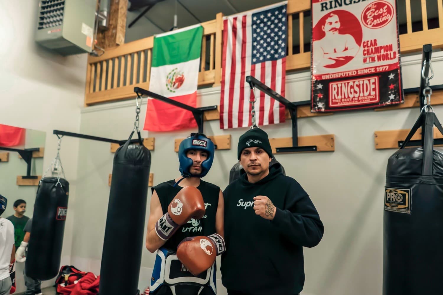 Coach Pablo with a fighter under the member flags at BoxFit Utah